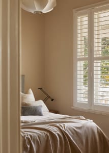 Minimalist bedroom featuring a bed with a lamp and window shutters.