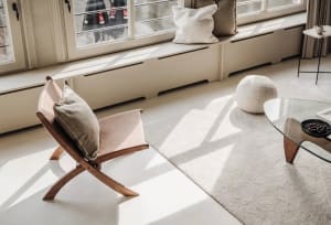 A minimalist interior design featuring a wooden chair with pillows on a white floor.