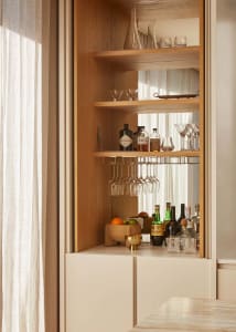 A modern bar station with wooden shelves containing various bottles and glasses.