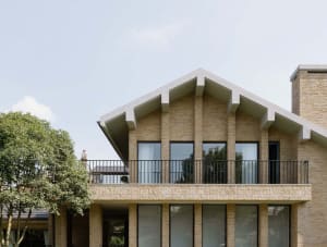A modern residential building with brick exterior, featuring large windows and a gable roof.