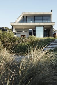 A modern house with a concrete and glass exterior, featuring a sleek, two-story design with large windows and a minimalist ae