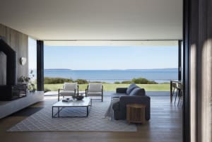 A modern living room with ocean views, featuring a sectional sofa, two armchairs, and a coffee table.