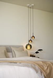 A modern bedroom featuring minimalist design with hanging pendant lights and neutral textiles, creating a cozy atmosphere.