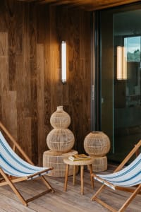 Modern wooden deck chairs and woven lanterns on a wooden floor.