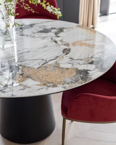 A modern dining room featuring a round marble table with a black base and red upholstered chairs.