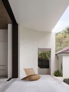 A modern exterior concrete patio with a unique curved chair and green plants.
