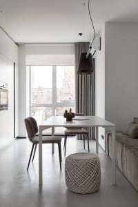 A modern minimalist living and dining room with a sleek white table and chairs, a large window, and a comfortable sofa.