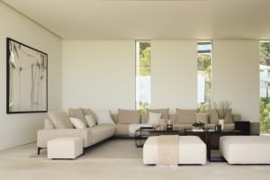 Modern minimalist living room with a large corner sofa, two ottomans, and a small coffee table.