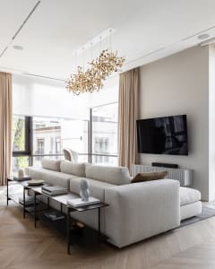 Modern minimalist living room with neutral-toned textured fabric sofa, black and gold coffee table, and large beige curtains 
