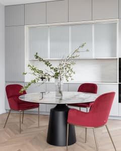 A modern dining room with a round marble table and red upholstered chairs.
