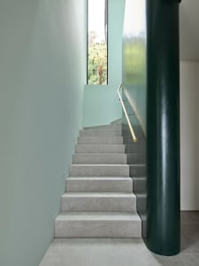 A modern staircase with concrete steps and metal handrail, featuring a green painted support column and a window showcasing f