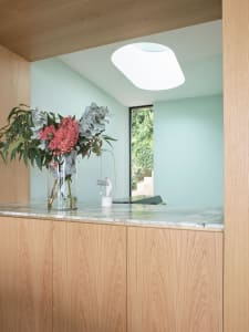 A modern, minimalist kitchen interior featuring wooden cabinets and a marble countertop with a vase of flowers.