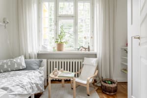 A minimalist bedroom with wooden furniture, white fabrics, and green plants.
