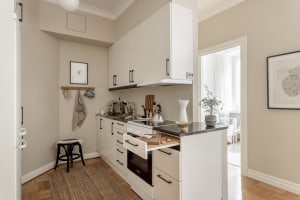 A spacious, modern, minimalist kitchen with white cabinets, a wood floor, and beige walls.