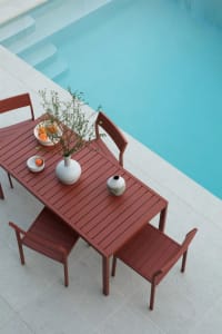 Modern outdoor patio furniture with metal table and chairs featuring plant and orange bowl.