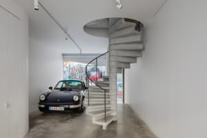 A modern garage with a black Porsche 911 parked next to a concrete spiral staircase.