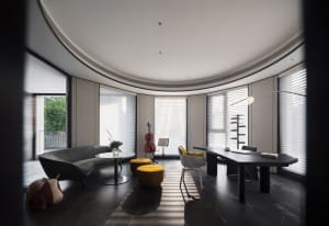 A modern, minimalist home office featuring sleek black furniture, large windows, and a visible cello.