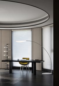 A modern office desk with a sleek design, minimalistic style, and a large window with blinds.