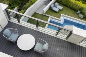 Modern patio with a round table and two chairs, featuring a concrete deck, glass railings, and a concrete wall with a glass w