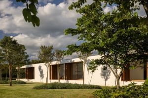 A modern residential building with white painted walls and concrete exterior, surrounded by greenery and tall trees.