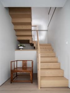 A minimalist staircase made of light-colored wood with a single wooden chair next to it.