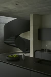 A modern minimalist kitchen with a spiral staircase in concrete.
