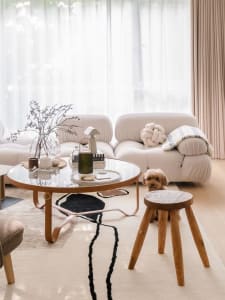 A cozy, modern minimalist living room with white textured fabric furniture, a wooden stool, and a glass coffee table adorned 