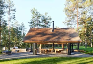 A modern residential patio pavilion with a straw roof, outdoor seating, and a fireplace.