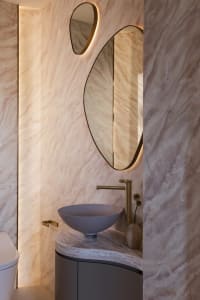 A modern bathroom with marble walls and a bowl-shaped sink.