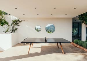 Minimalist patio featuring a concrete ping pong table with a mountainous backdrop through circular windows.