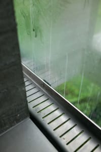 A metallic drain channel with a grid pattern along the bottom edge, installed indoors.