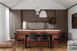A modern residential kitchen with wood cabinets, a stainless steel backsplash, and a black dining table with black chairs.