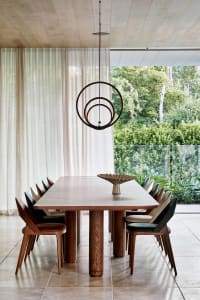 Modern dining room featuring a wooden table with a unique pendant light hanging above, surrounded by multi-colored chairs and