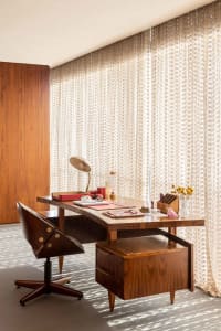 A modern industrial home office with a wooden desk and swivel chair, featuring a red desk organizer and a lamp.