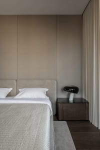 A modern minimalist bedroom with a neutral color palette, featuring a sleek upholstered bed, a dark wood bedside table with a