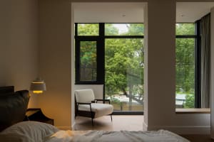 A cozy, minimalist bedroom with a white fabric armchair overlooking green trees.