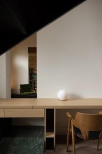 Modern home office featuring a minimalist wooden desk with a white spherical object and a retro green chair, against white wa