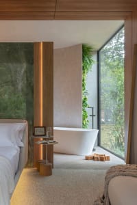 A minimalist bedroom with a marble wall, wooden accents, and a large window overlooking trees.