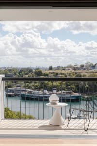 A modern balcony featuring a metal table and chair, with a scenic river view and ships in the background.