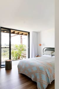 A modern bedroom featuring wooden flooring and a bed with a blue and beige patterned blanket.