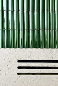 Green tiled wall with a white concrete base featuring horizontal slits.