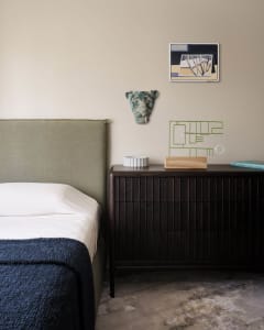 A minimalist bedroom featuring wooden furniture, a green headboard, and a side table with decorative items.