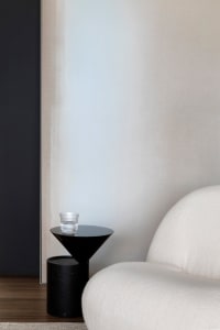 A minimalistic living room featuring a sleek, modern white sofa and a black side table with a single glass tumbler.