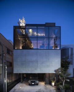 A minimalist house with a concrete base and glass walls at night.