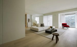 A minimalist living room with a white marble floor, white modular sofa, and red accent chair.