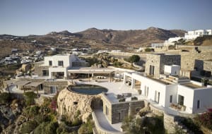 Modern residential exterior featuring white stucco and stone walls, a curved patio with a circular pool, and a terrace overlo