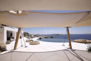 A modern residential patio featuring concrete flooring, a circular seating area, an infinity pool, and scenic ocean views.