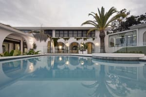 A modern residential exterior featuring a white stucco exterior with large windows, arched doorways, and a palm tree by the p