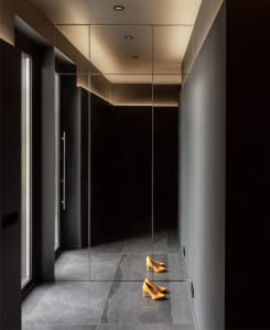Orange high-heeled shoes reflected on a minimalist mirror in an interior space.