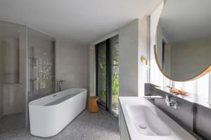 A modern minimalist bathroom featuring a white freestanding bathtub, a large sink area, and a glass shower enclosure, with co